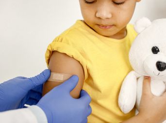 Childhood-vaccinations Child holding a teddy bear while receiving a vaccination with a bandage on the arm