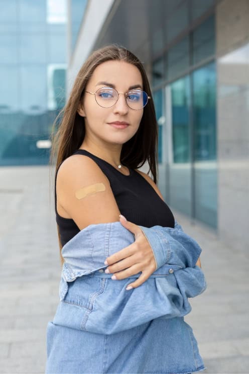 Immunisation-adult Woman with a bandage on her arm after vaccination, standing in front of a building